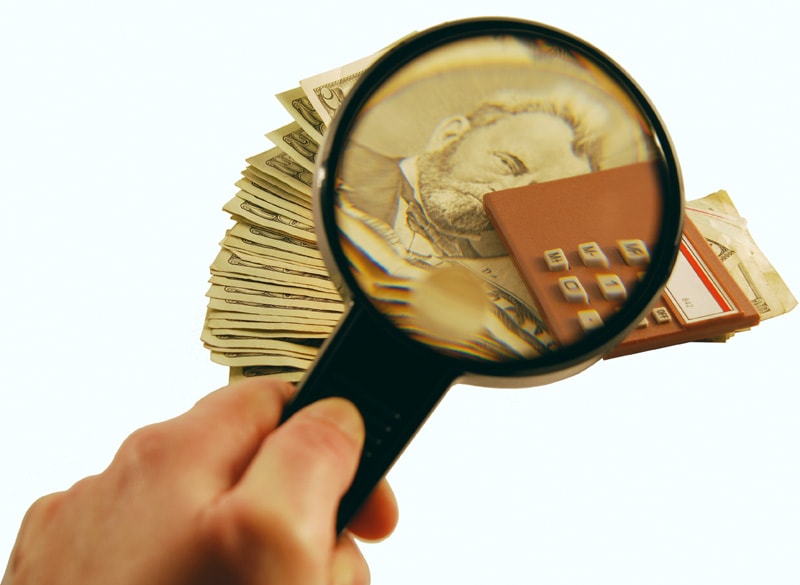 A magnifying glass over a stack of cash, showing how it's worth reviewing how your strategic plan and fundraising plan work together.