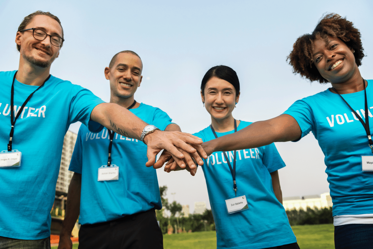 A group of volunteers puts their hands together in a field to celebrate the contributions that quality volunteers make to nonprofits