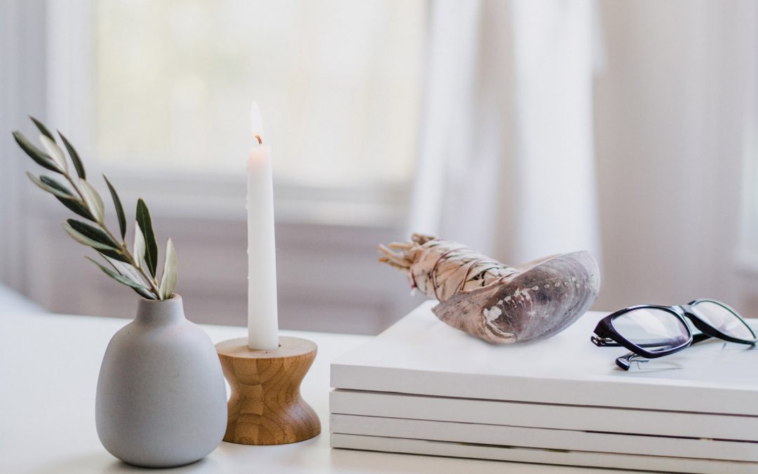 A bud vase with a branch, a lit candle, and a pair of glasses sitting on a table, projecting the kind of serenity many leaders hope to find through coaching.