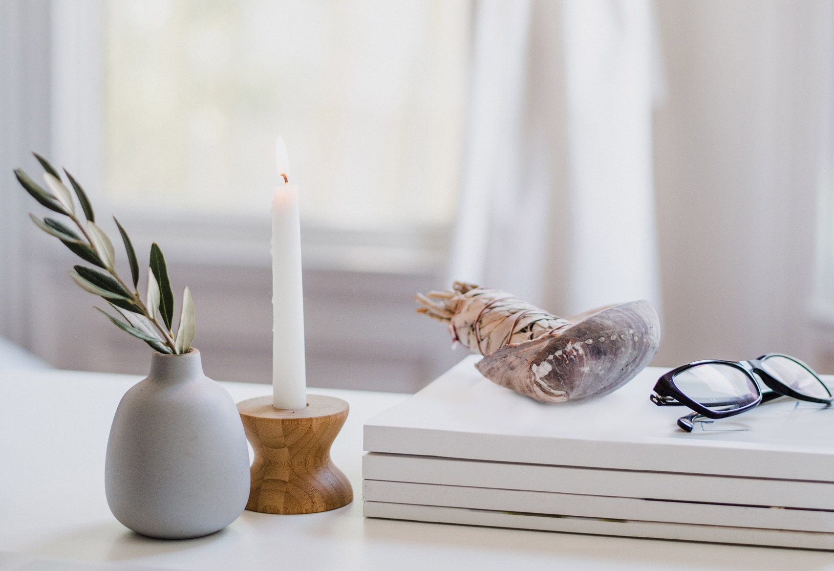 A bud vase with a branch, a lit candle, and a pair of glasses sitting on a table, projecting the kind of serenity many leaders hope to find through coaching.