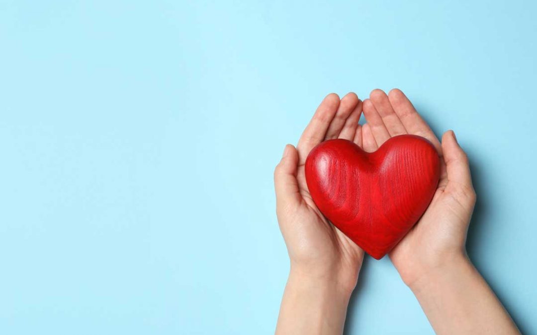 A pair of hands holding a heart on a blue background, showing how creating a sustainable nonprofit requires a focus on not just money but impact.