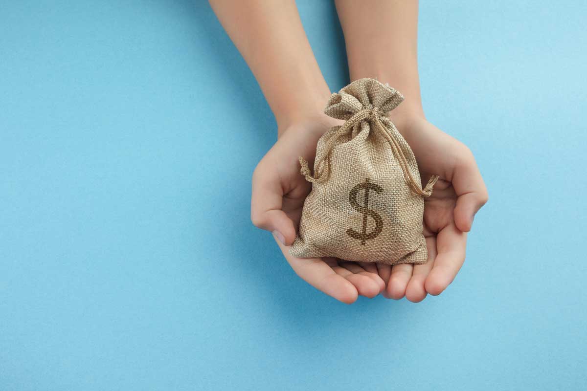 Two hands holding a small burlap bag with a dollar sign on it, against a blue background, showing why a good donor communications strategy is so important.