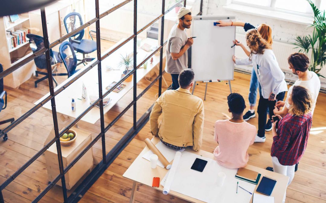 A group of employees in an open office floor plan discussing how the rapidly evolving business environment requires the management of expectations and a focus on adaptability.