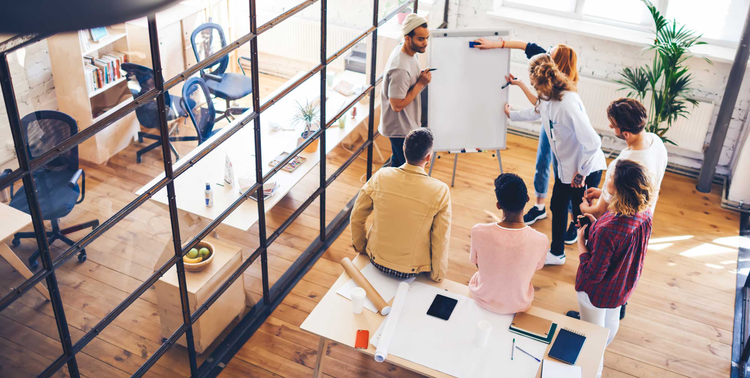 A group of employees in an open office floor plan discussing how the rapidly evolving business environment requires the management of expectations and a focus on adaptability.