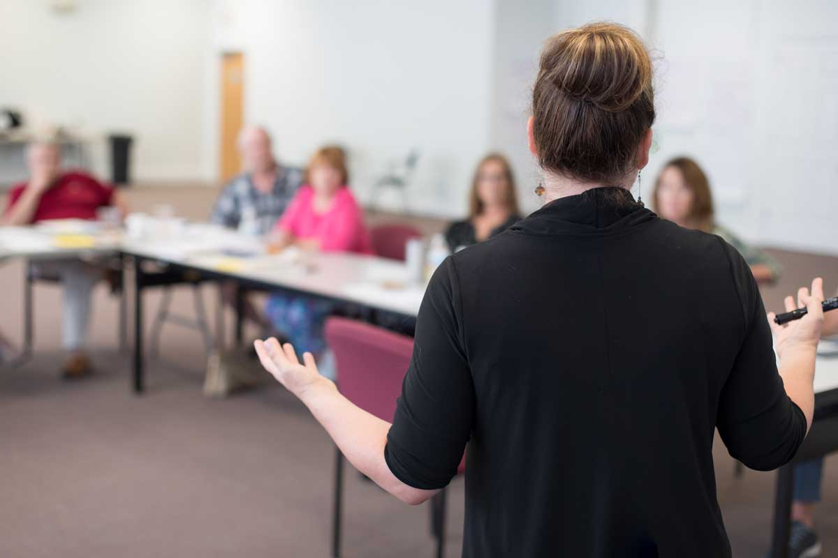 A person in a black sweater speaking to a group of stakeholders, facilitating a strategic visioning session.